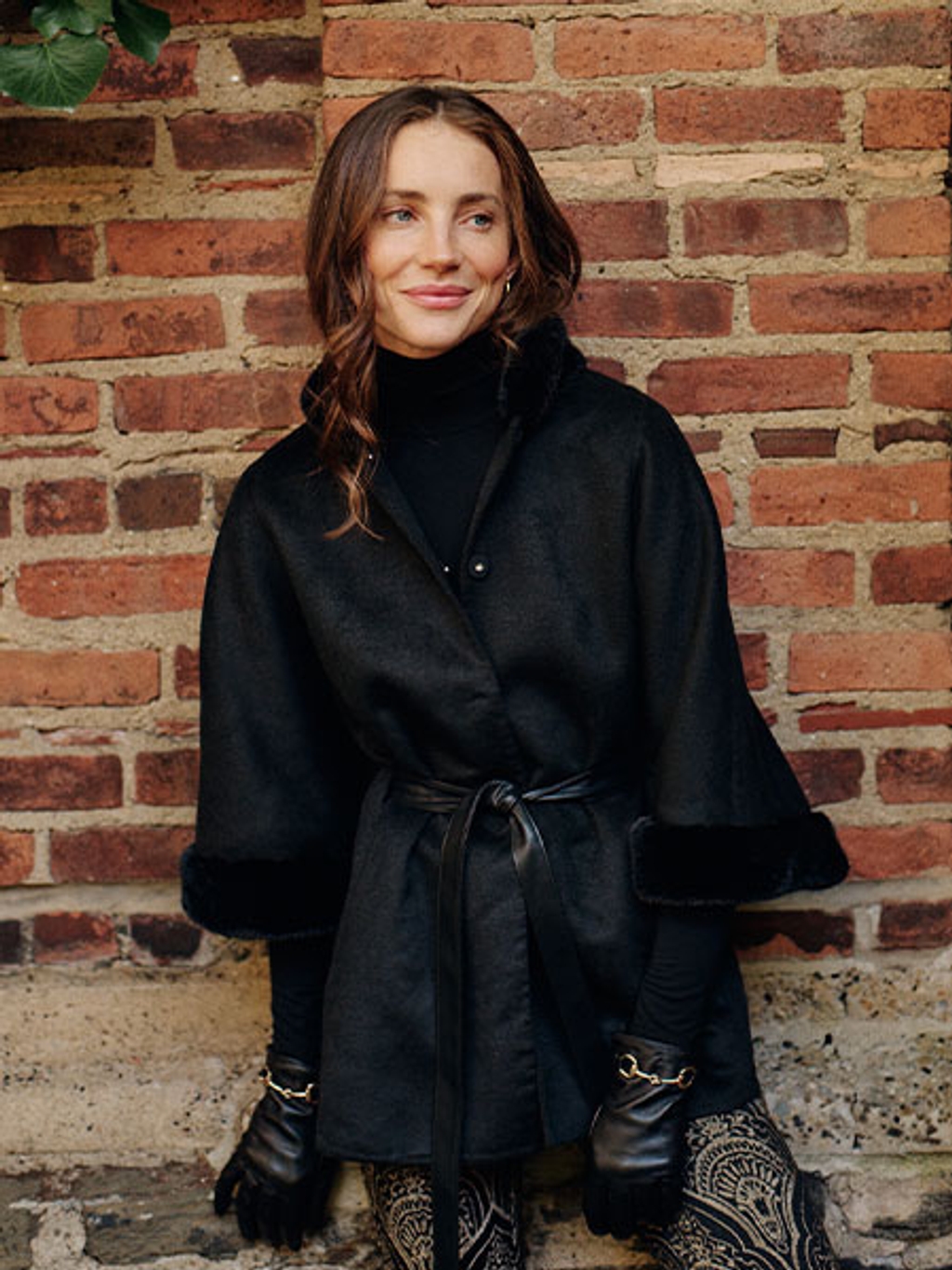 Model in black poncho, black turtleneck, and gold jacquard pants Model in black poncho, black turtleneck, and gold jacquard pants