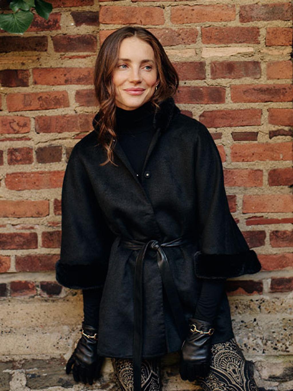 Model in black poncho, black turtleneck, and gold jacquard pants Model in black poncho, black turtleneck, and gold jacquard pants
