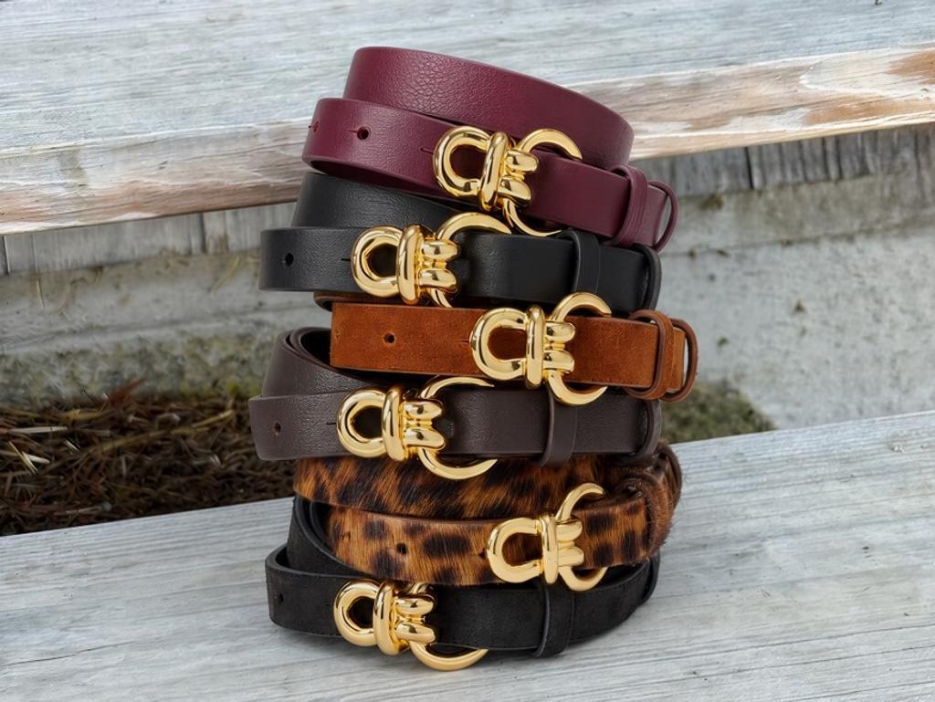 A stack of seven belts in various colors, each with a gold horseshoe-shaped buckle.