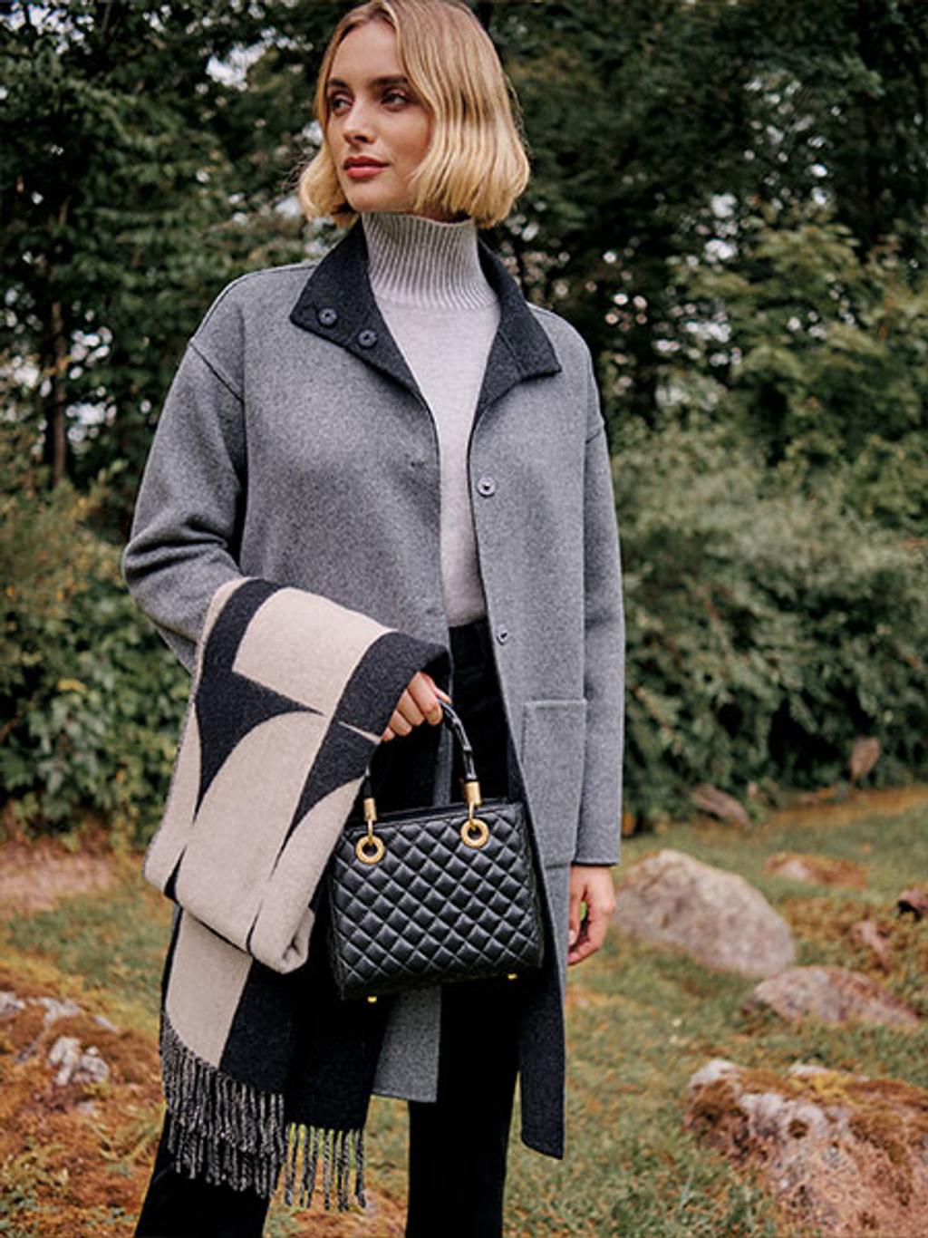 Female model wearing a gray coat and holding a black handbag and scarf.
