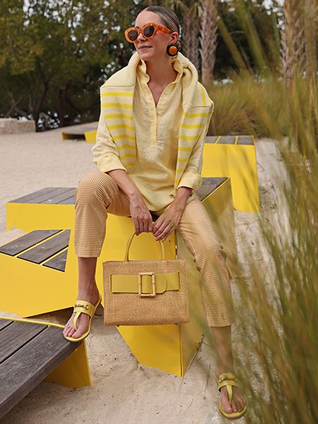 Influencer, Blaire Edie, sitting on. yellow outdoor bench wearing yellow gingham  pants, yellow sandal and yellow and white stripe shirt in the lula style