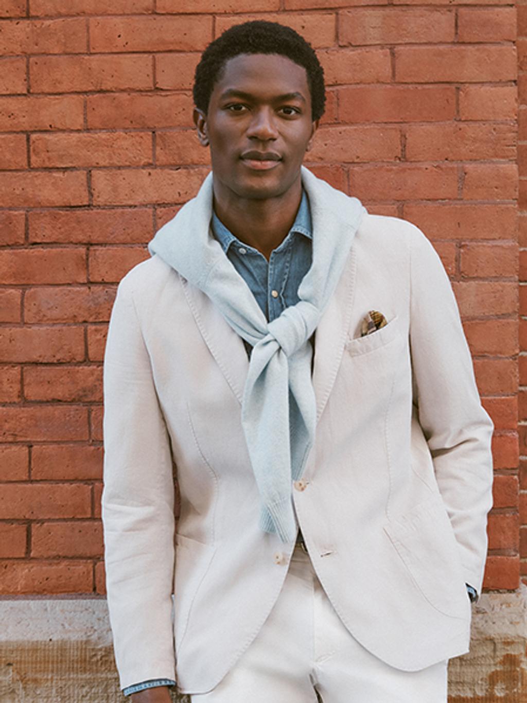 Man wearing a stylish ensemble, with a white sports coat and a sweater tied over the shoulders.