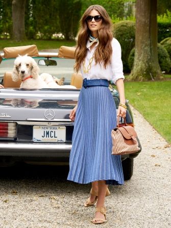 woman standing outside by a car wearing navy pleated longer skirt