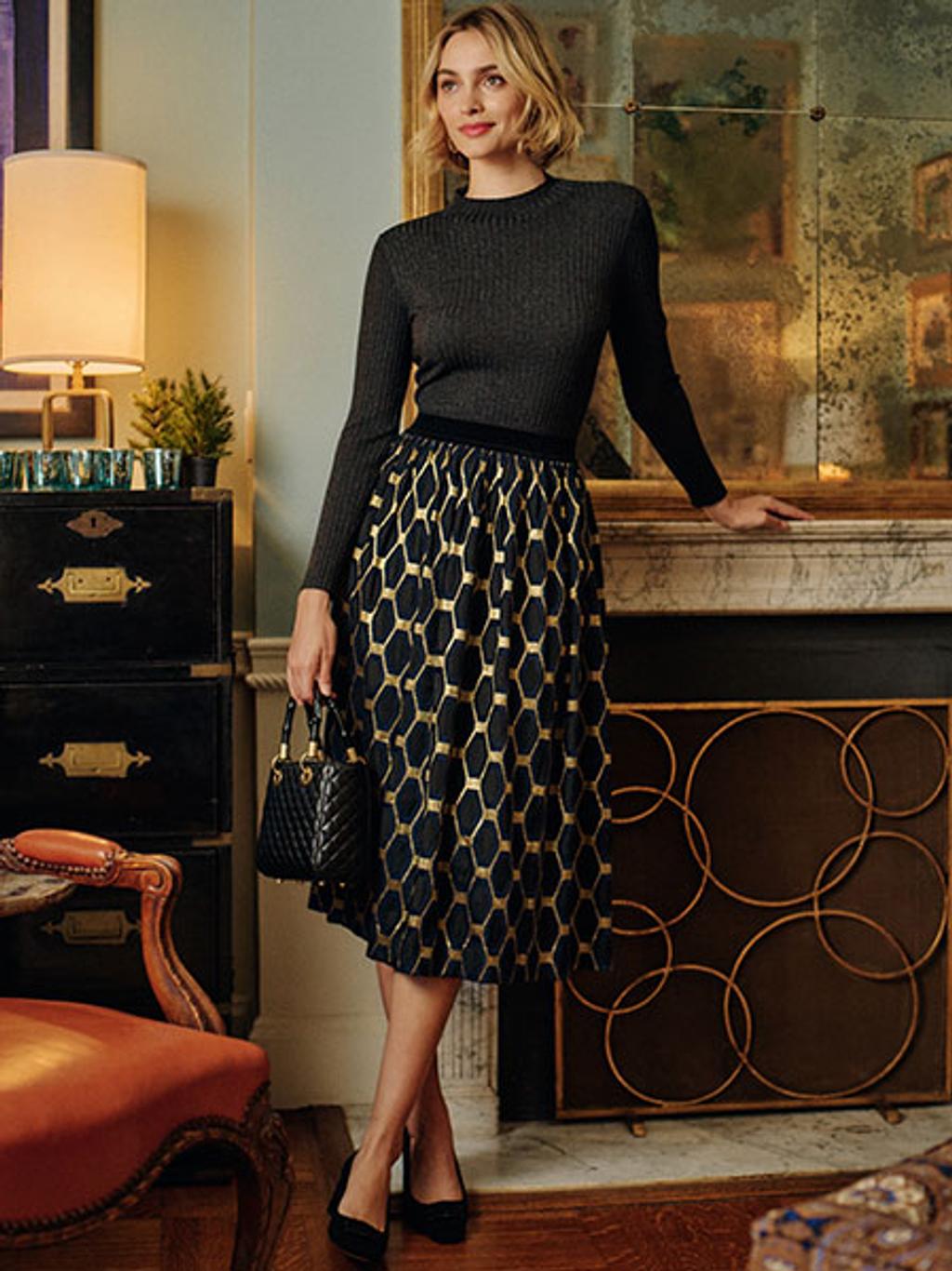 Model wearing rib-knit turtleneck, jacquard skirt, and heels in front of fireplace Model wearing rib-knit turtleneck, jacquard skirt, and heels in front of fireplace