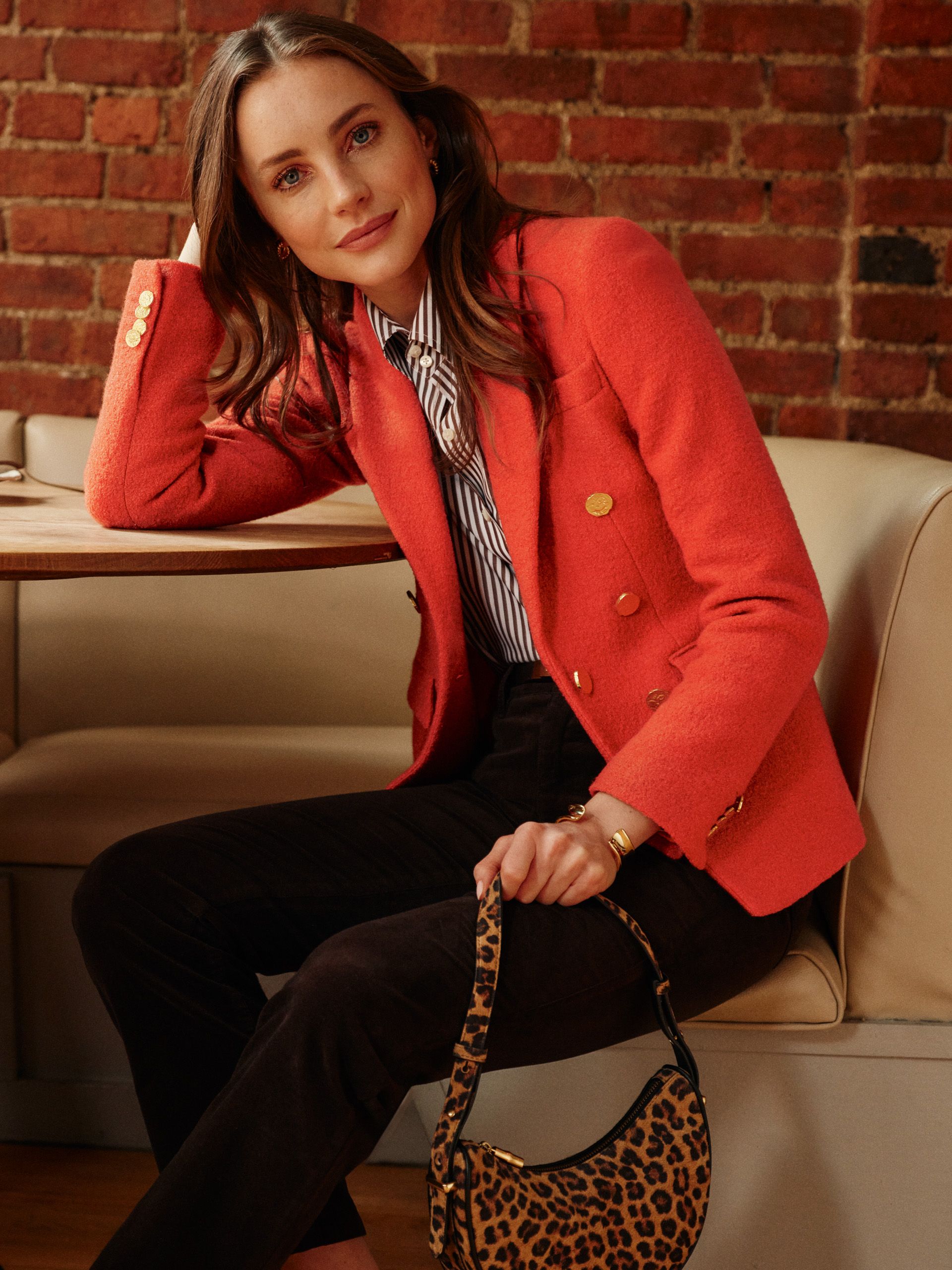 woman seated in restaurant booth wearing orange boucle blazer and holding animal pattern bag
