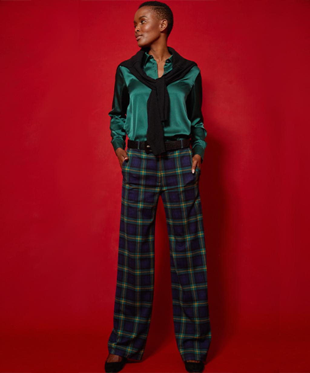 Model wearing tartan pants, satin button-down, cashmere sweater, leather belt, and suede pumps.