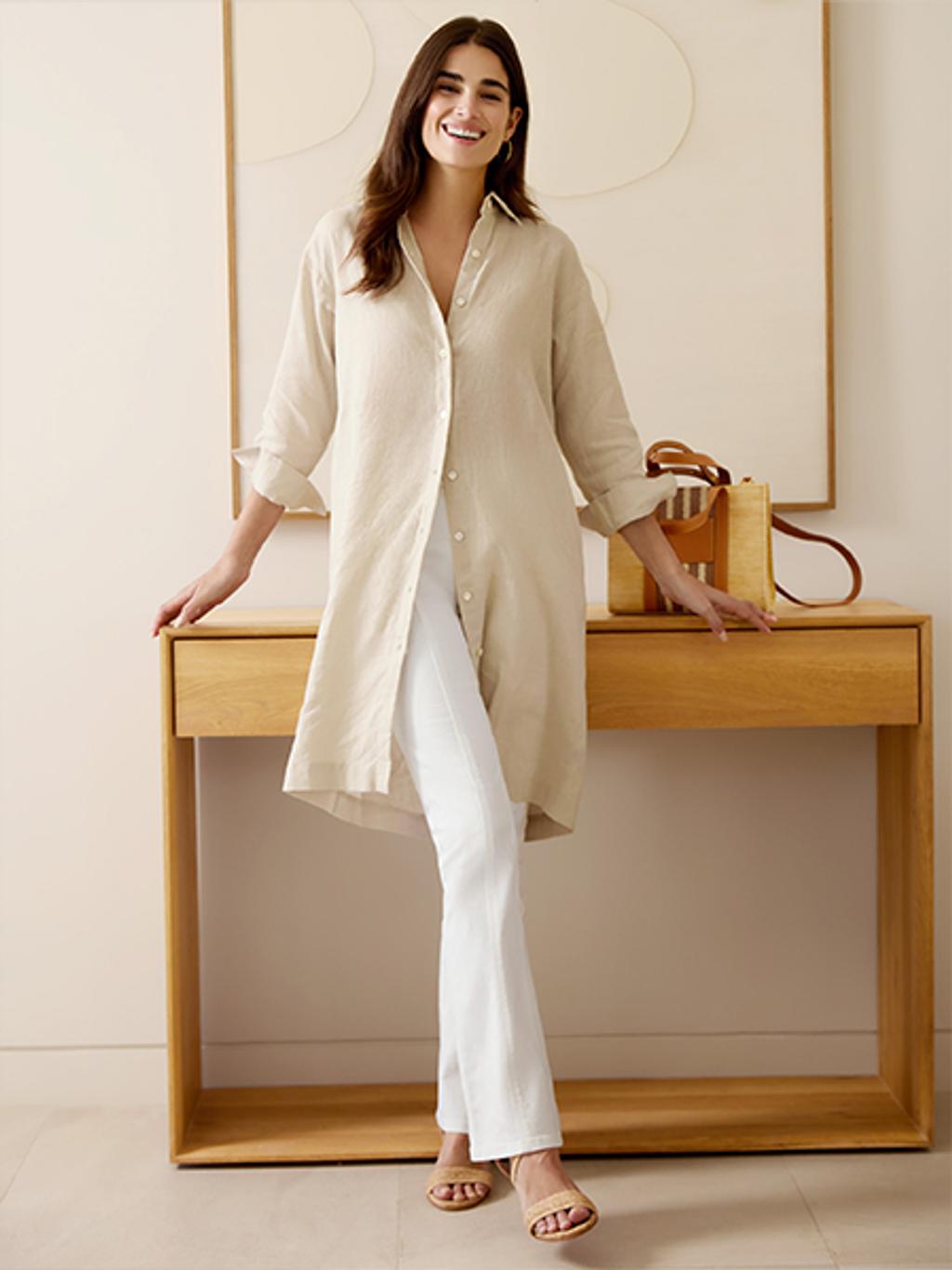 Woman wearing beige button up linen tunic and white pants, paired with strappy leather sandals.
