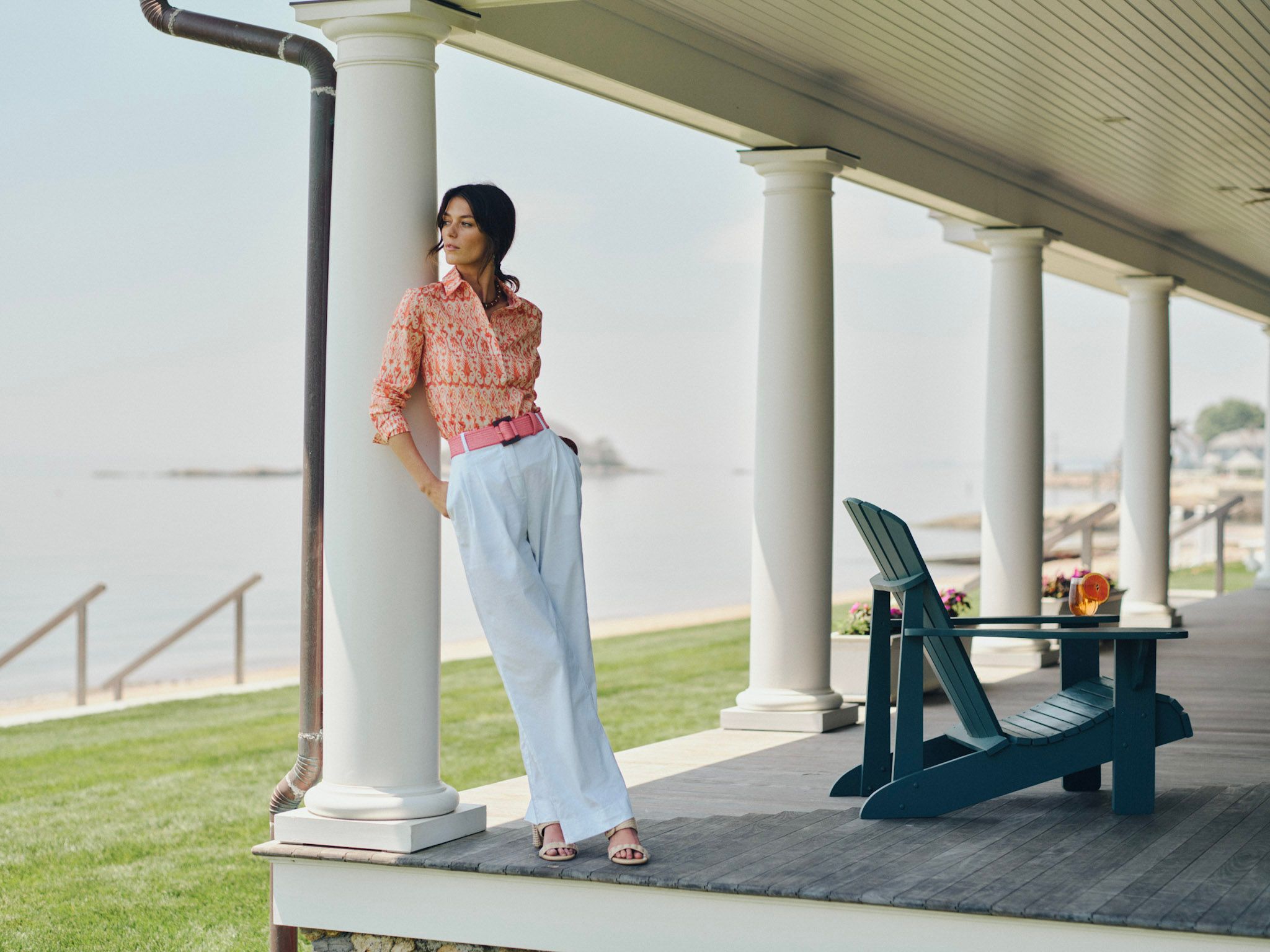 A woman on a porch, leaning against a white column, overlooking the sea.