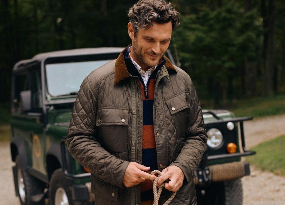 man walking outside away from a car wearing an olive quilted jacket and a navy and burgundy style rugby stripe sweater