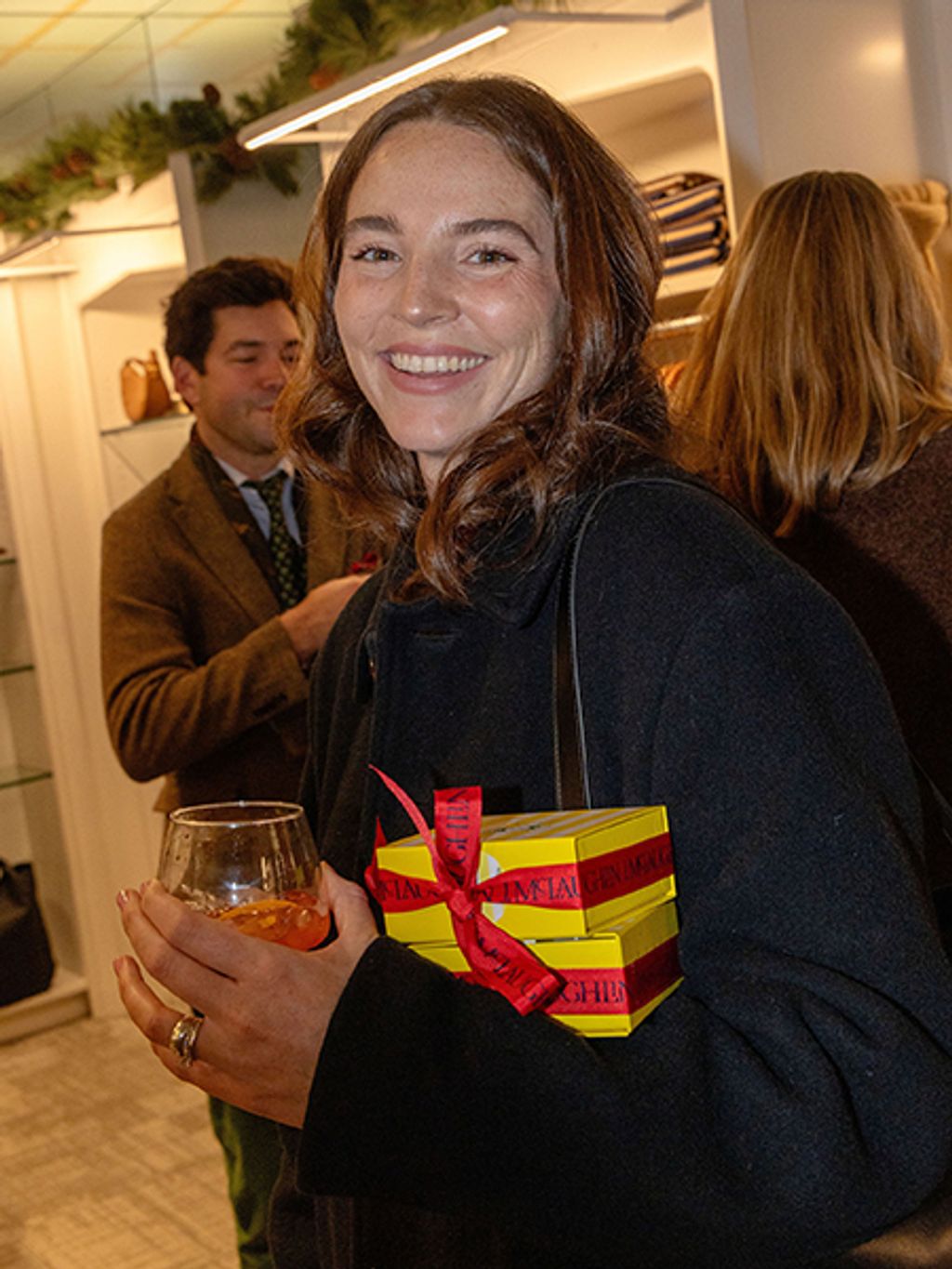 Smiling woman posing with presents and a drink in hand.