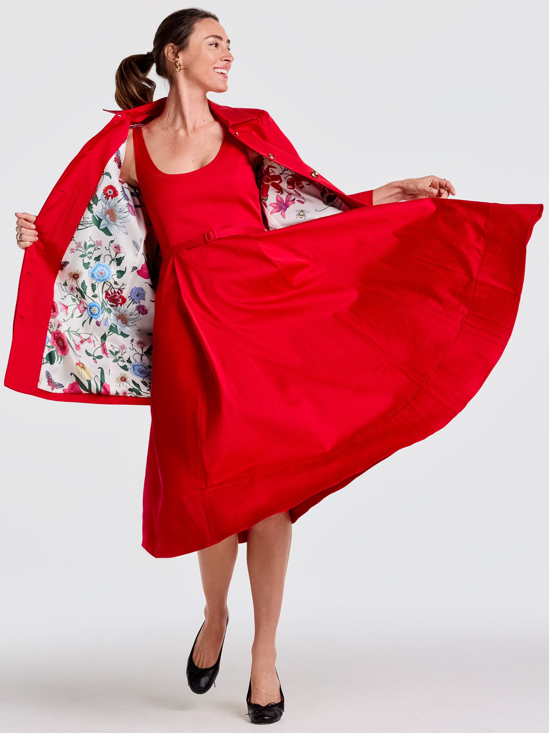 Smiling woman in a red dress and red floral-lined trench coat, posing dynamically.
