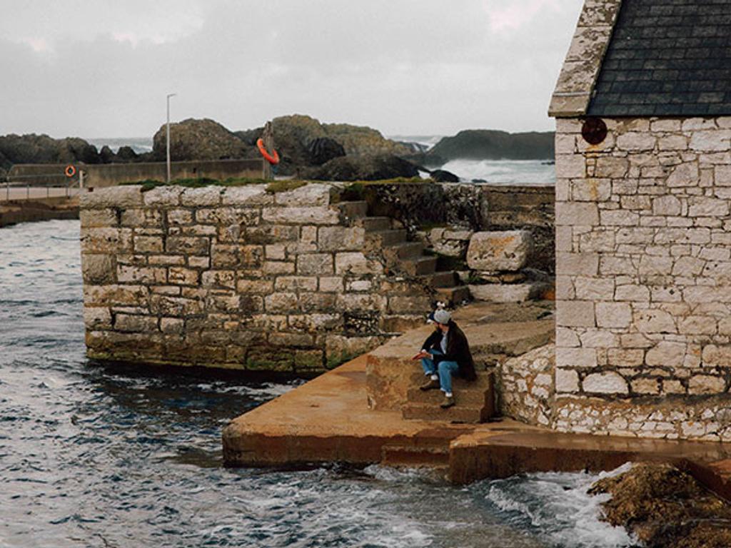 Jamie sits on a dock wearing the Corduroy Suffolk jacket in Olive