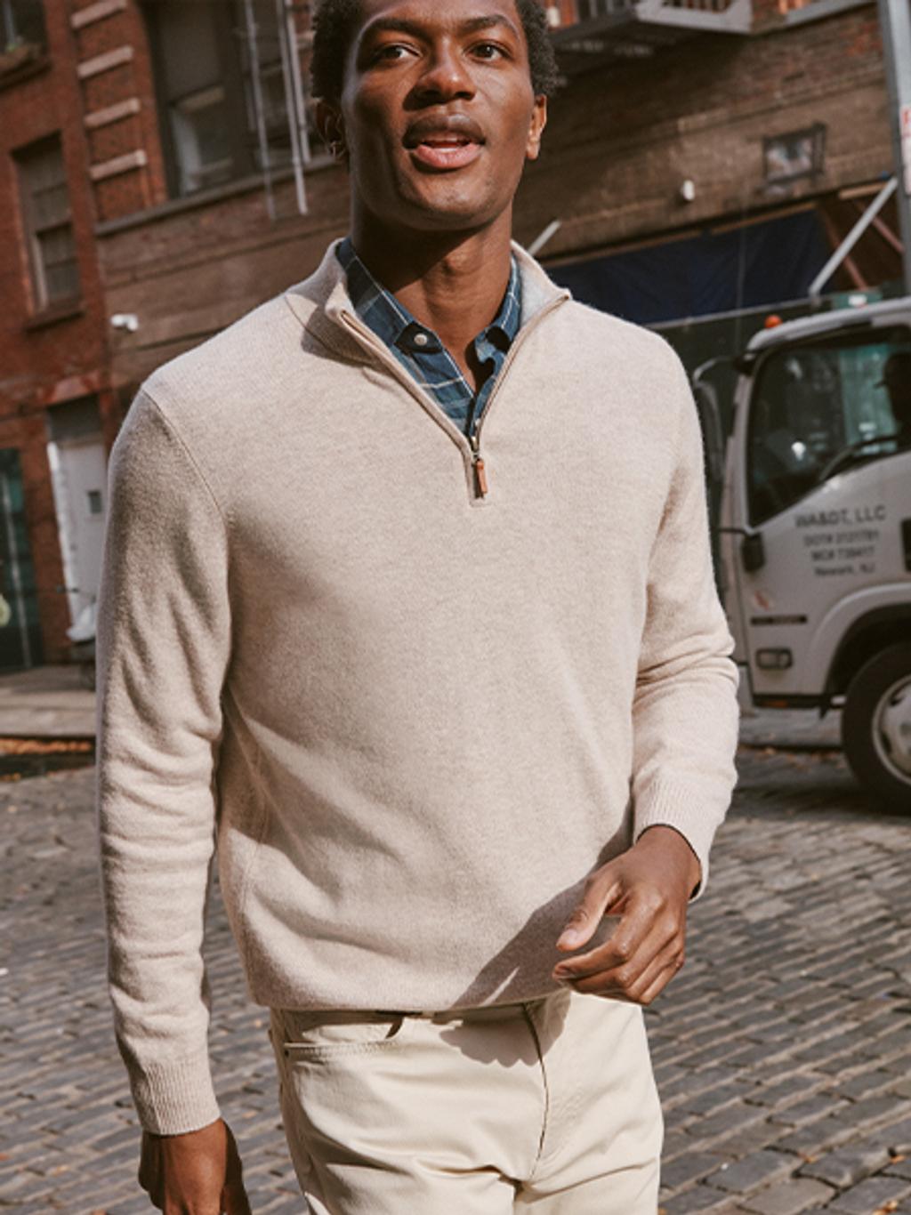 Man walking down the street wearing a cream quarter zip sweater with a button down shirt underneath.