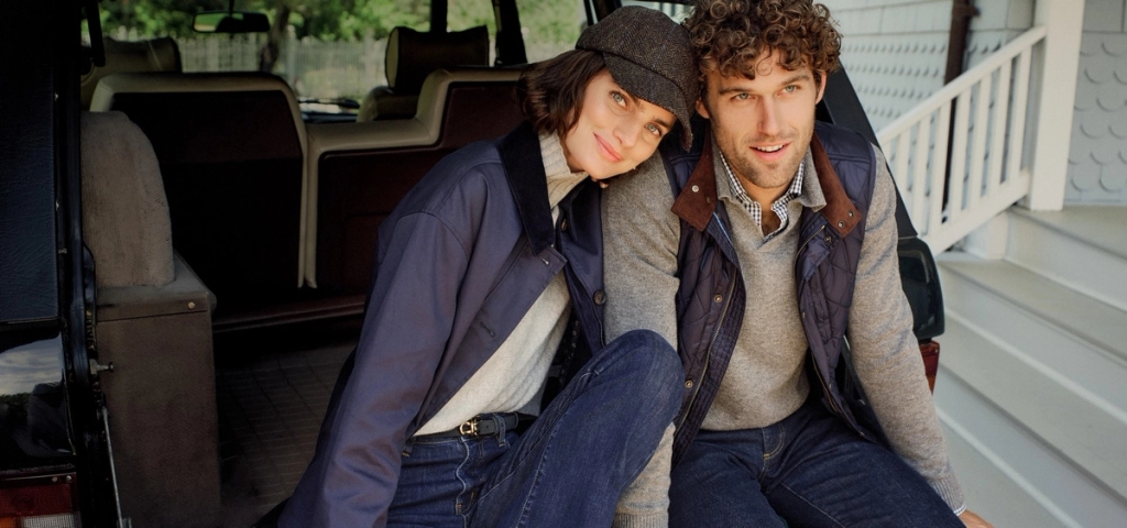 A smiling man and woman in casual autumn attire sit in the back of an open SUV, the woman leaning on the man's shoulder.