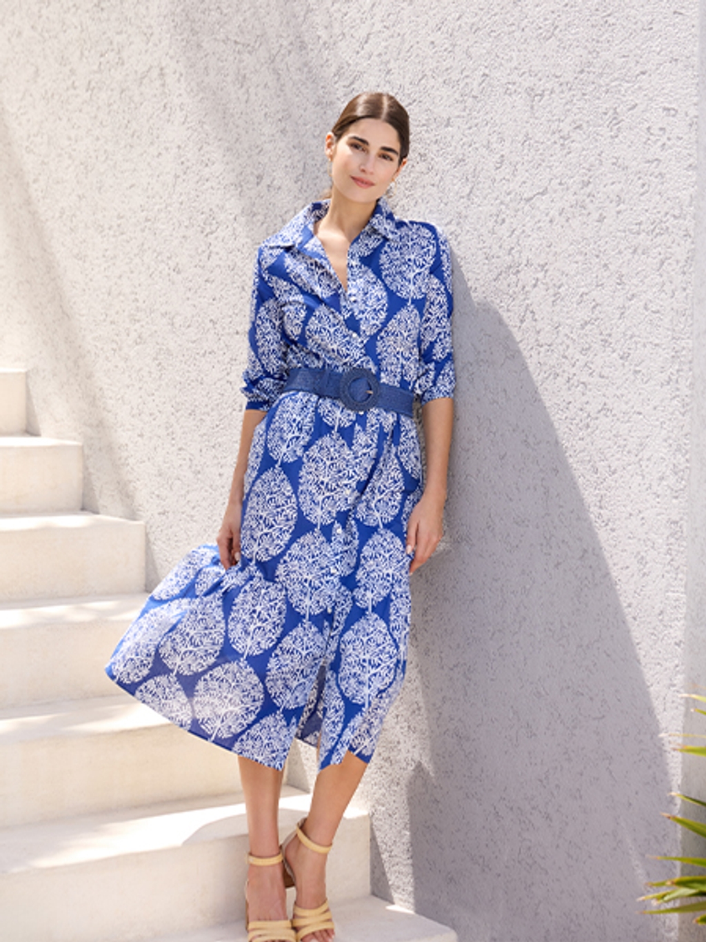 Woman in blue floral dress, blue belt, and tan sandals