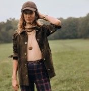 woman standing in field wearing camel ribbed turtleneck and olive green suede jacket