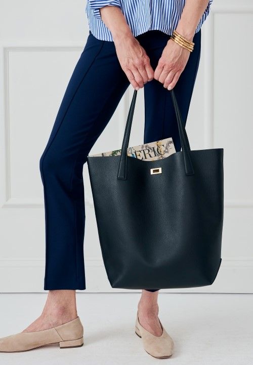 cropped image of woman holding black large leather tote bag with turnlock closure, standing in front of white studio backdrop