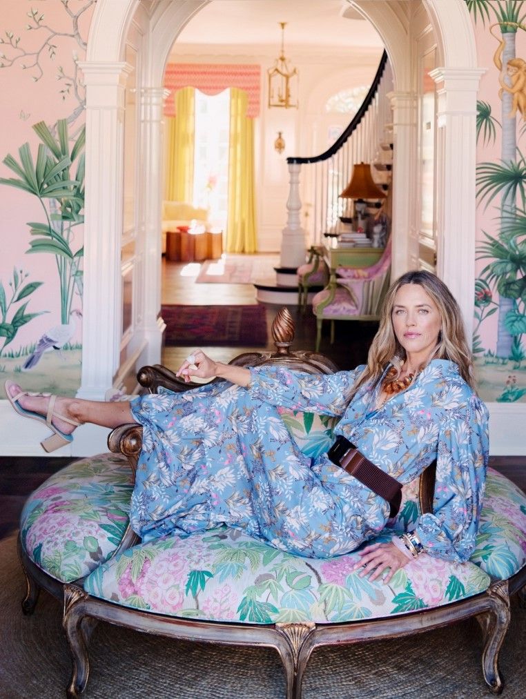 woman seated inside on a large floral pattern ottoman wearing a blue gloral printed dress