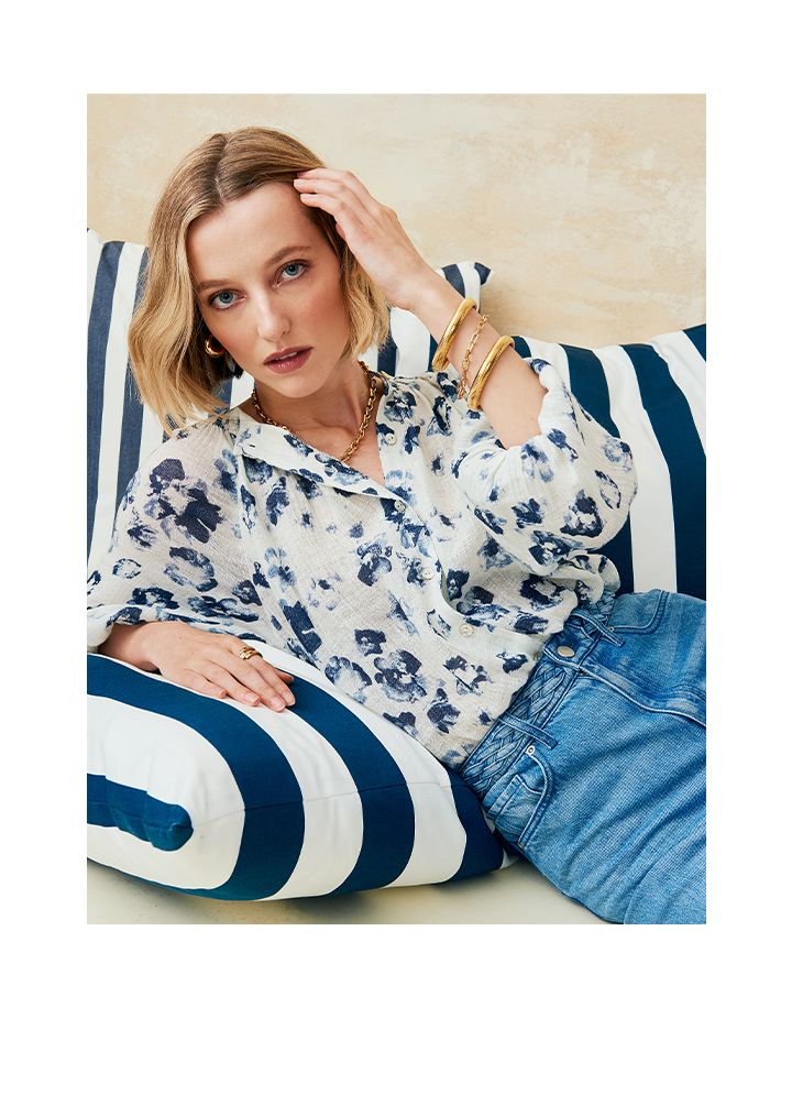 Woman leaning on striped pillows wearing a blue printed blouse.