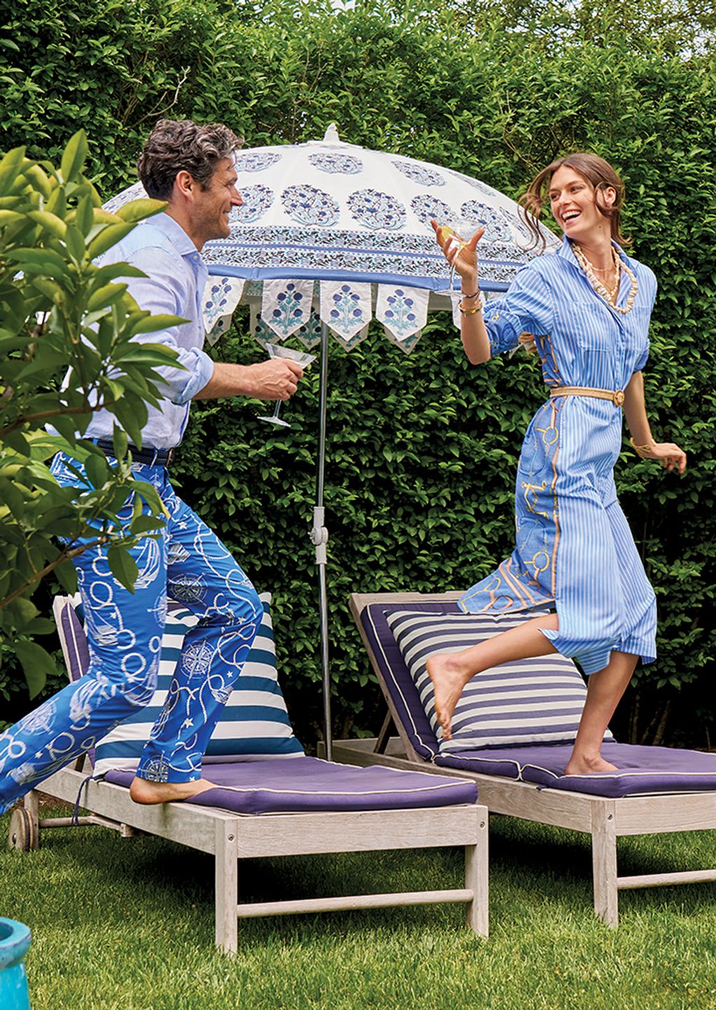 Man and women standing on beach chair with drink in hand wearing a striped shirt dress.