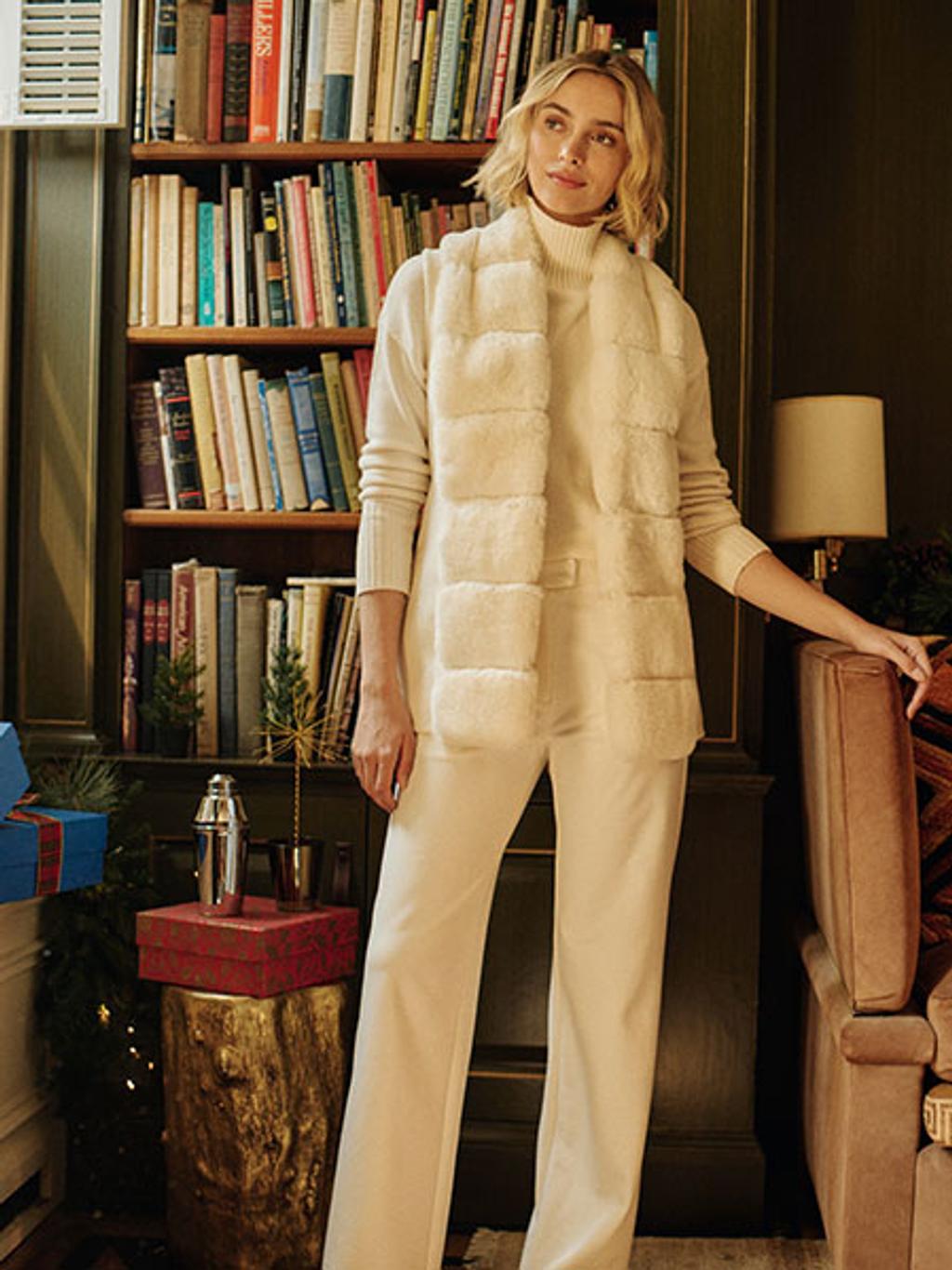 Model wearing white outfit with white faux-fur vest Model wearing white outfit with white faux-fur vest