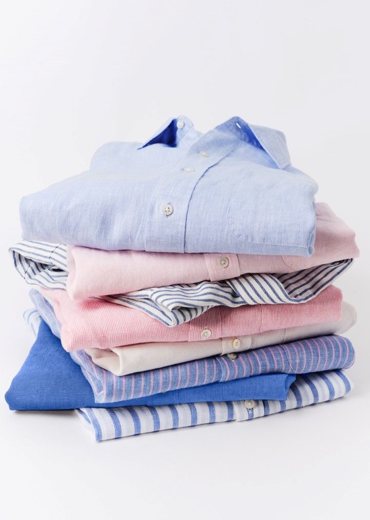 A stack of neatly folded shirts in shades of blue, pink, and white, some with stripes.