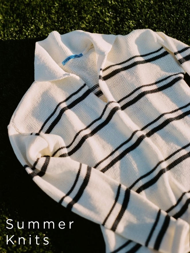 still life image of white polo sweater with navy stripes positioned on the grass