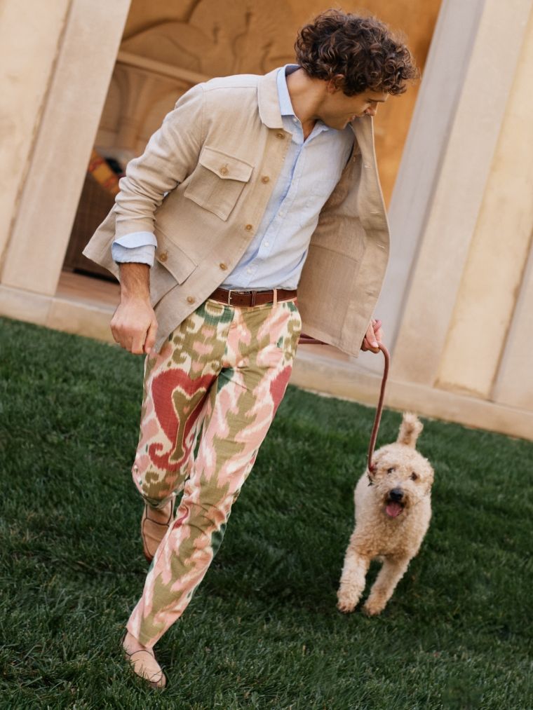 man walking with dog outside wearing multicolor floral pattern pants and beige jacket