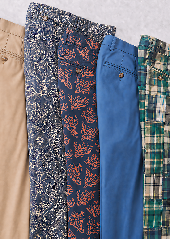 Five folded men's shorts: khaki, dark blue paisley, dark blue coral, royal blue, and green plaid.