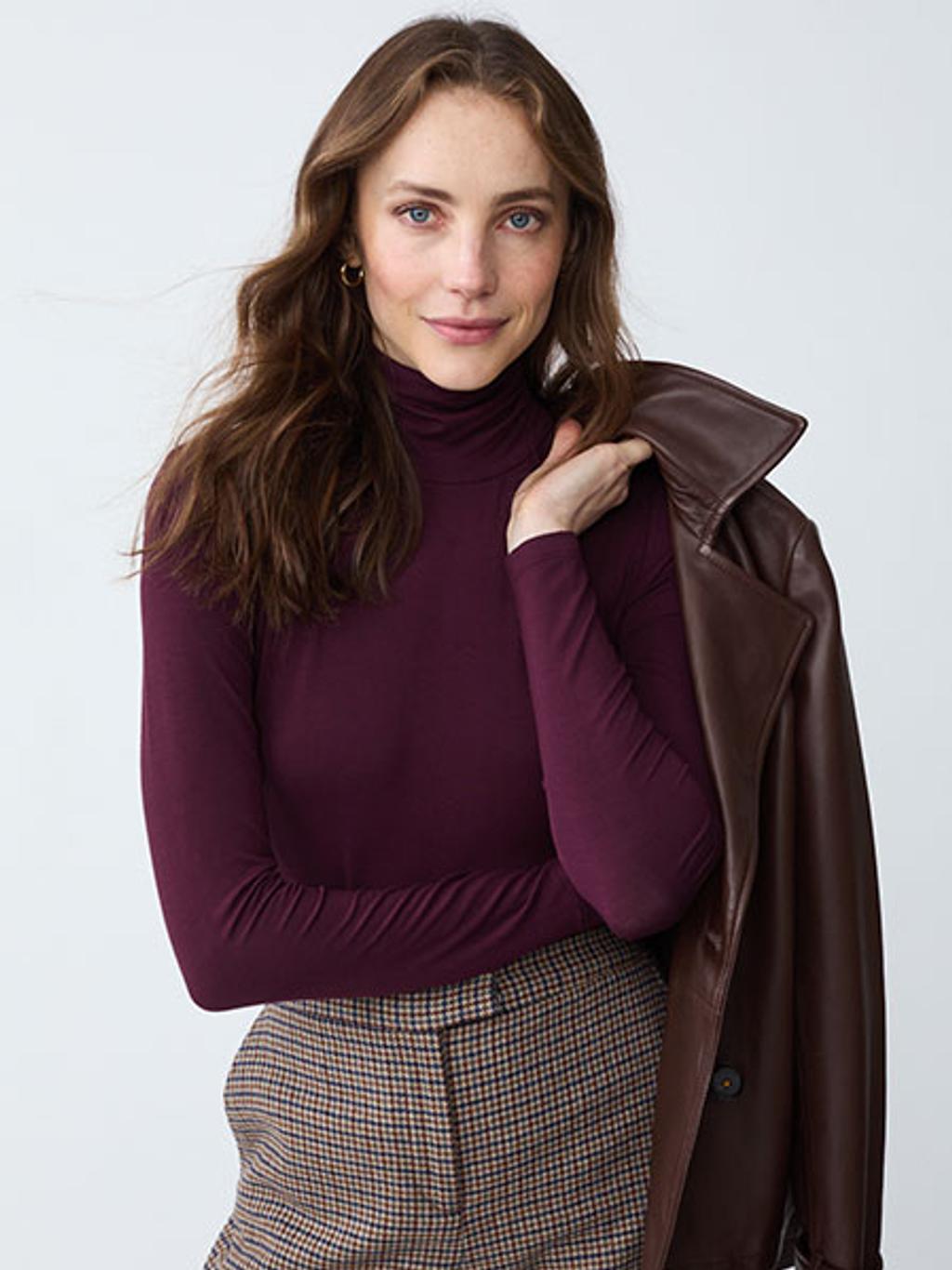 Model wearing burgundy turtleneck with leather jacket and plaid pants.