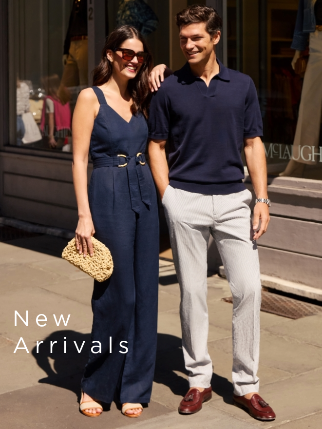 man and woman standing on the street during the day. She is wearing navy linen sleeveless jumpsuit and on him a navy knit polo and light gray slacks