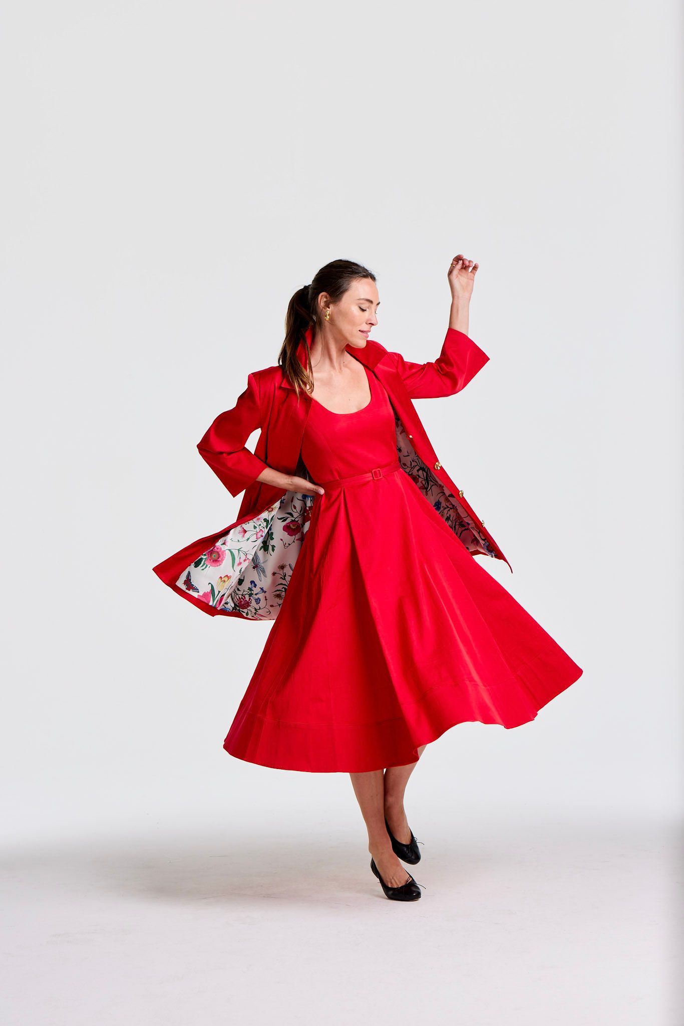 Elegant woman in a red dress and matching jacket with a floral lining, twirling.