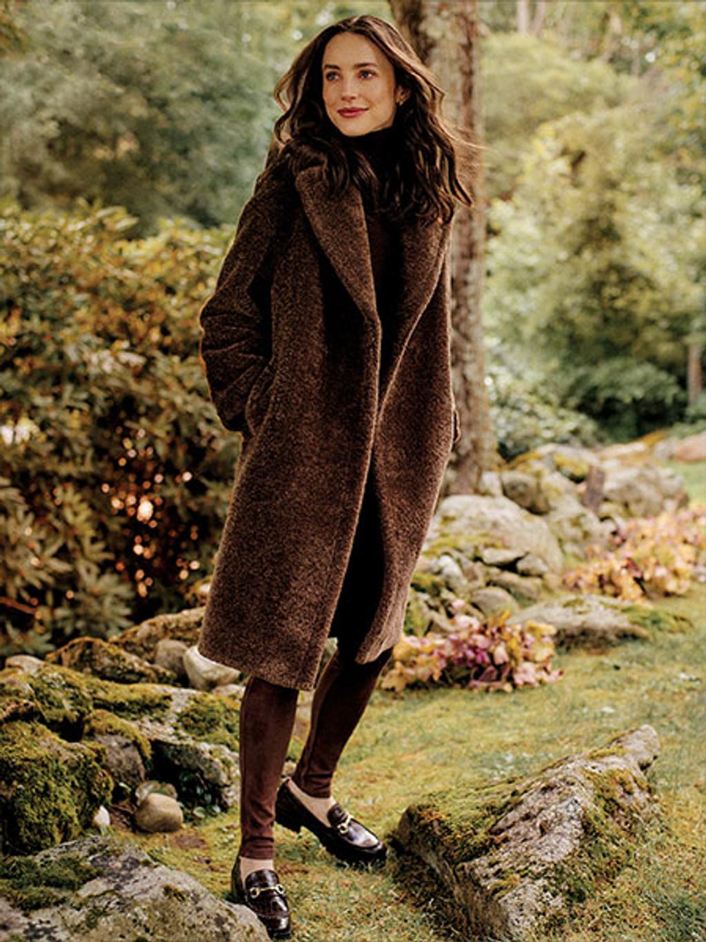 Brunette model wearing a full lenth brown faux fur coat.