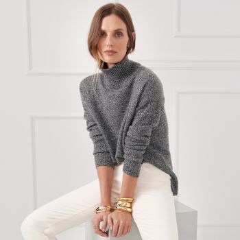 cropped in image of woman seated on white square block wearing egret white jeans and a heather charcoal cashmere turtleneck sweater