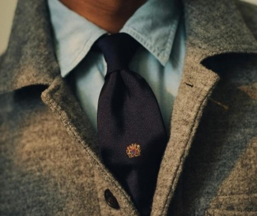 Grey jacket, light blue shirt, and navy tie with a small crest.