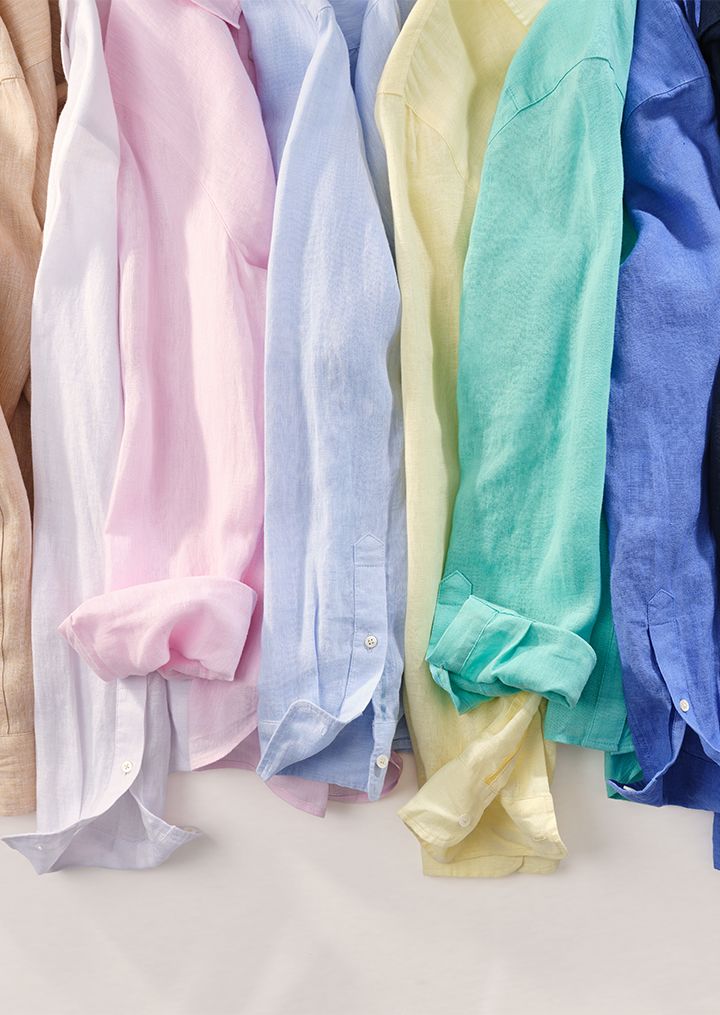 A close-up of a row of linen shirts in various colors, some with rolled sleeves.