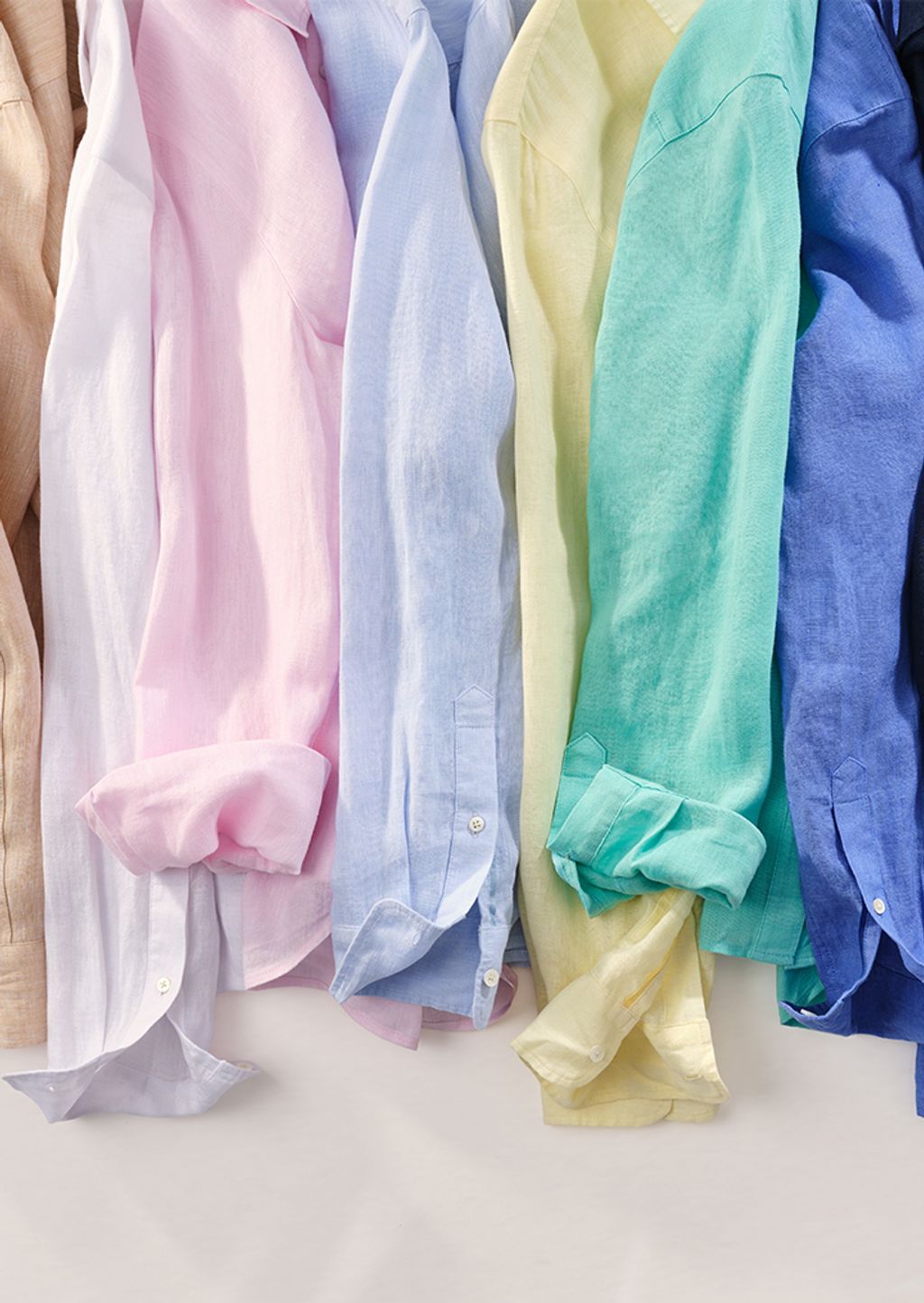 A close-up of a row of linen shirts in various colors, some with rolled sleeves.