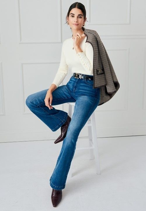 woman sitting on a stool wearing medium wash denim jeans and off white crewneck sweater