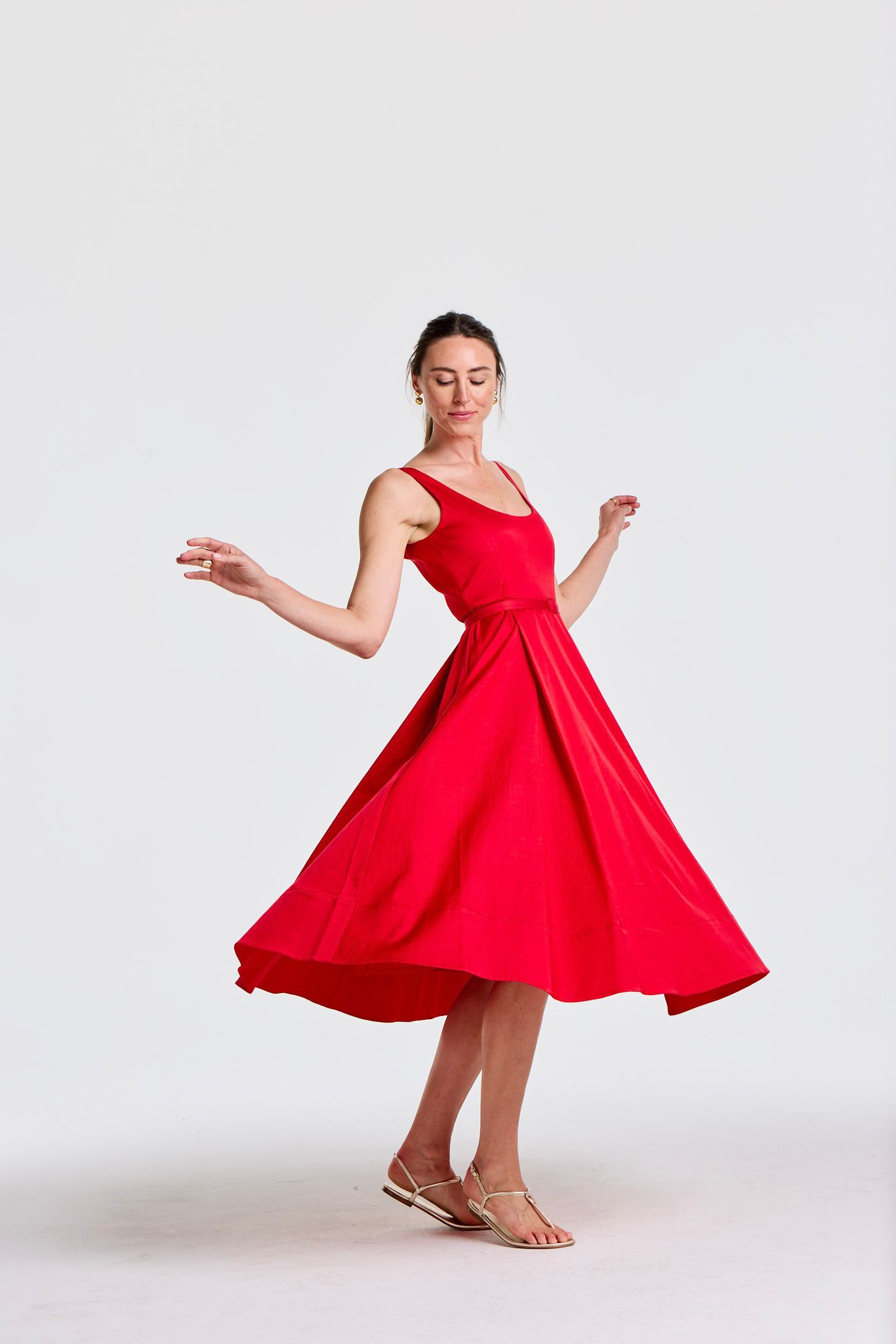 A woman in a vibrant red dress twirls, its full skirt flaring out, on a white background.