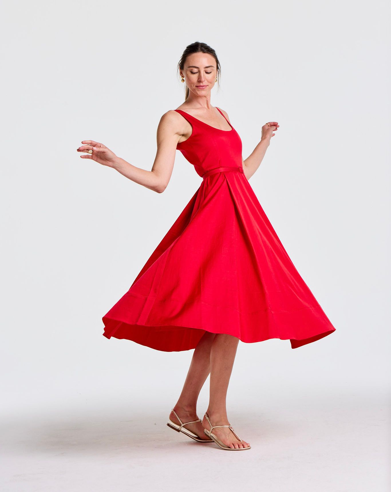 A woman in a vibrant red dress twirls, its full skirt flaring out, on a white background.