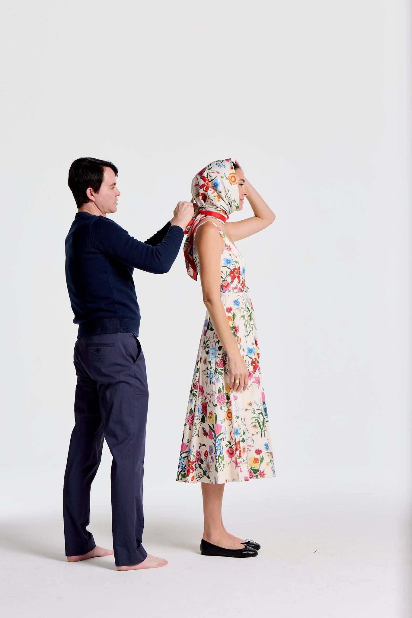 A man ties a floral headscarf on a woman wearing a floral dress.
