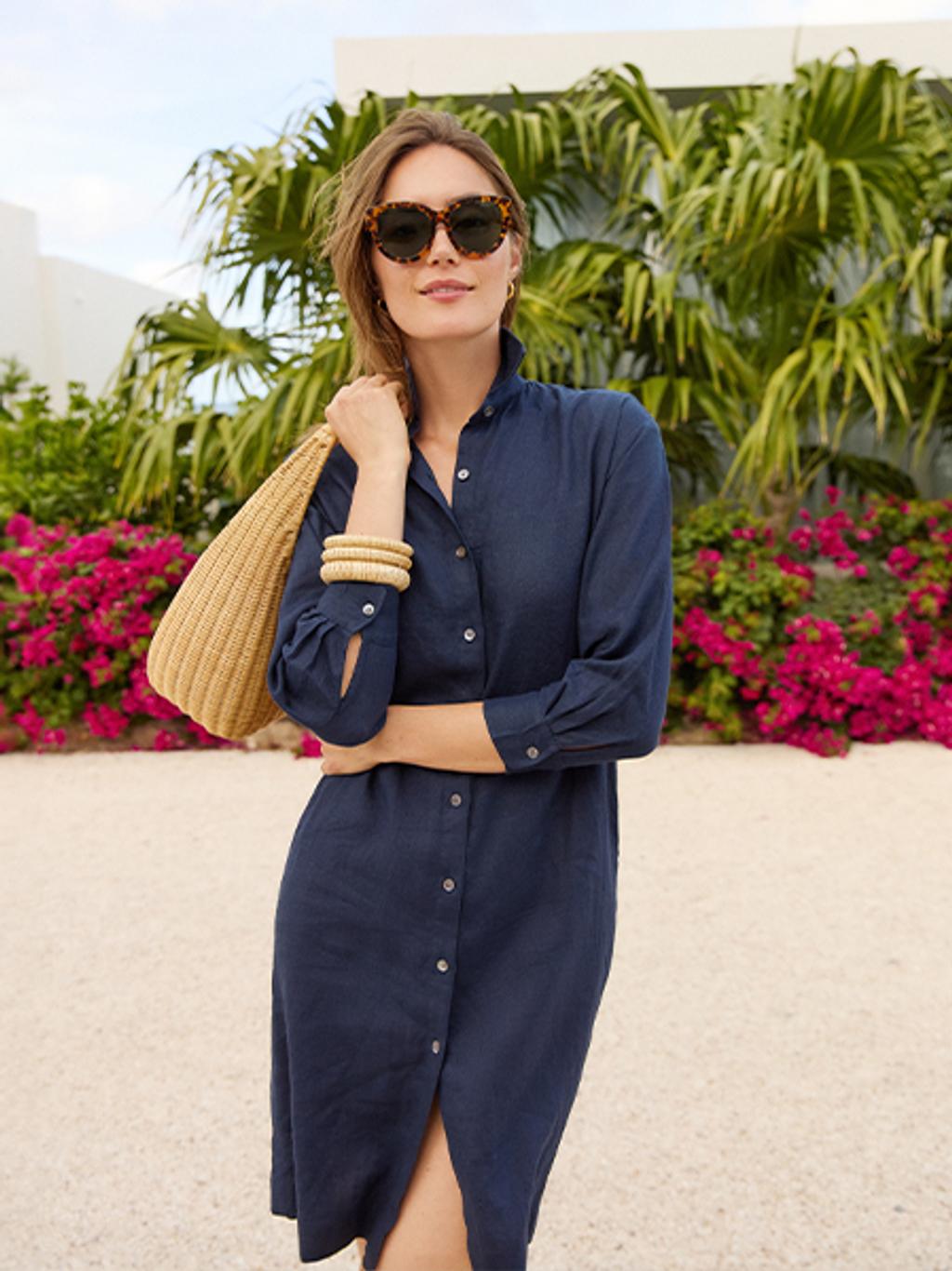 Woman in navy dress wearing brown sunglasses and carrying a wicker purse.