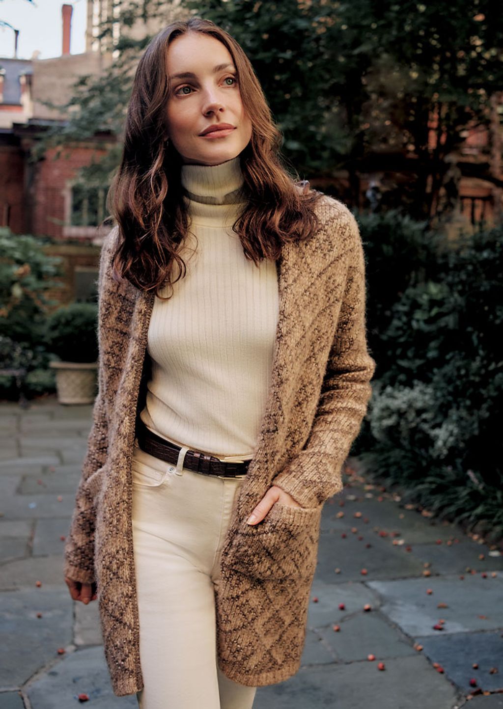 A woman wearing a beige jacquard sweater, an off white turtleneck, brown leather belt and off white jeans.