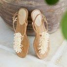 neutral leather and white beaded sandals standing upright in front of neutral backdrop