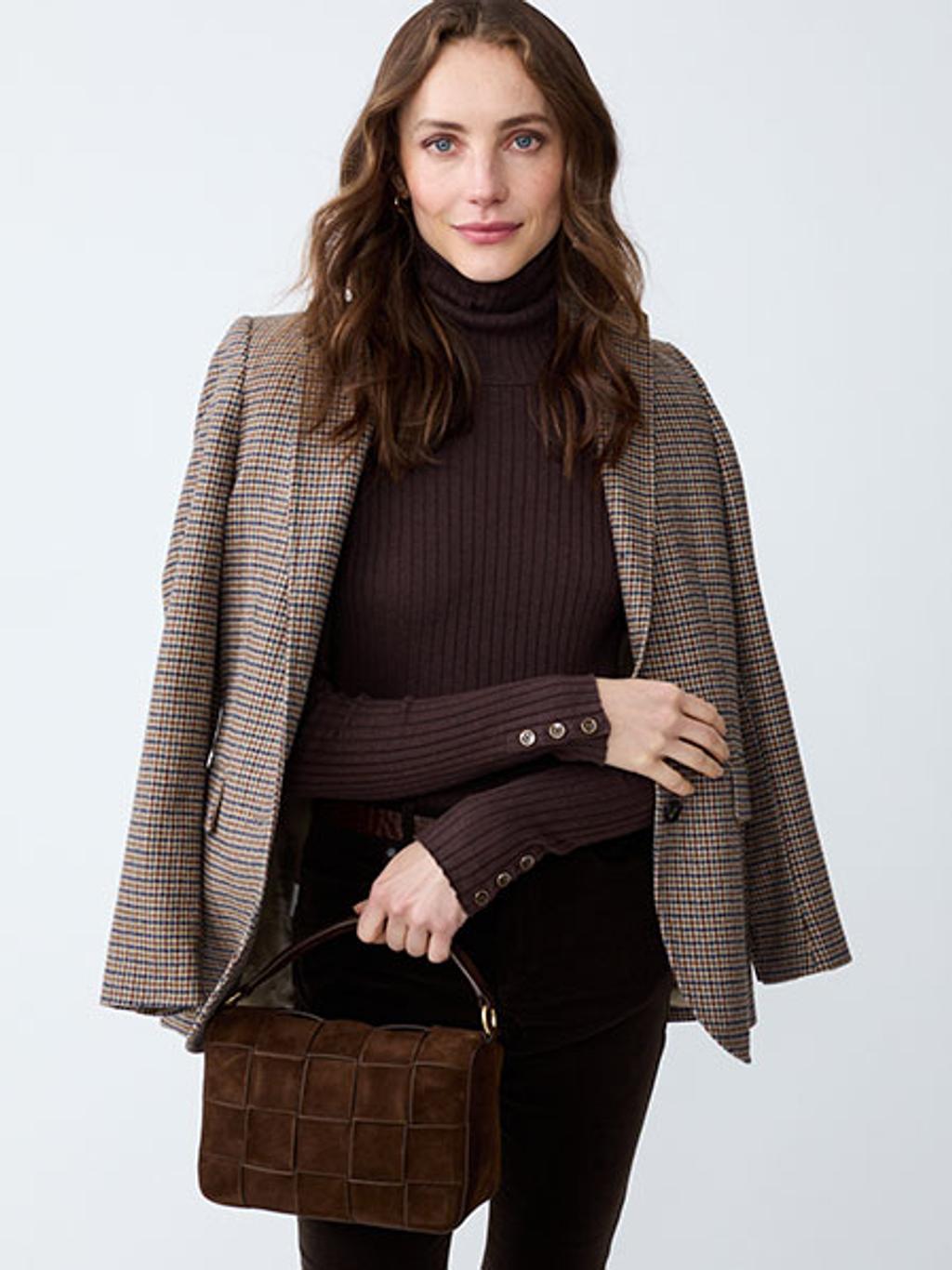 Model wearing a blazer and turtleneck carrying a woven top-handle bag Model wearing a blazer and turtleneck carrying a woven top-handle bag