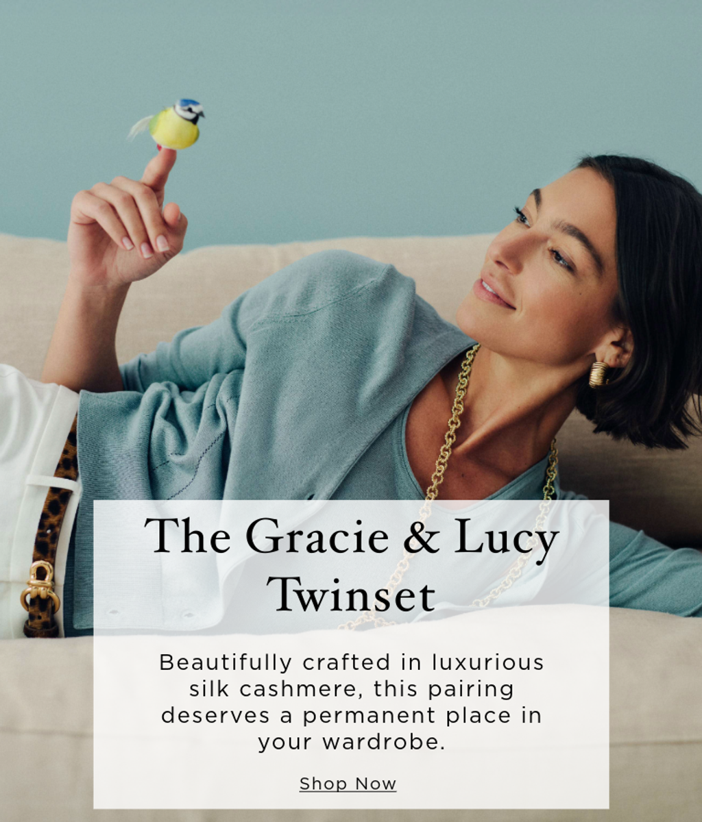 A woman in a light blue twinset reclines on a couch, looking at a toy bird perched on her finger. Overlay text: The Gracie & Lucy Twinset. Shop Now.