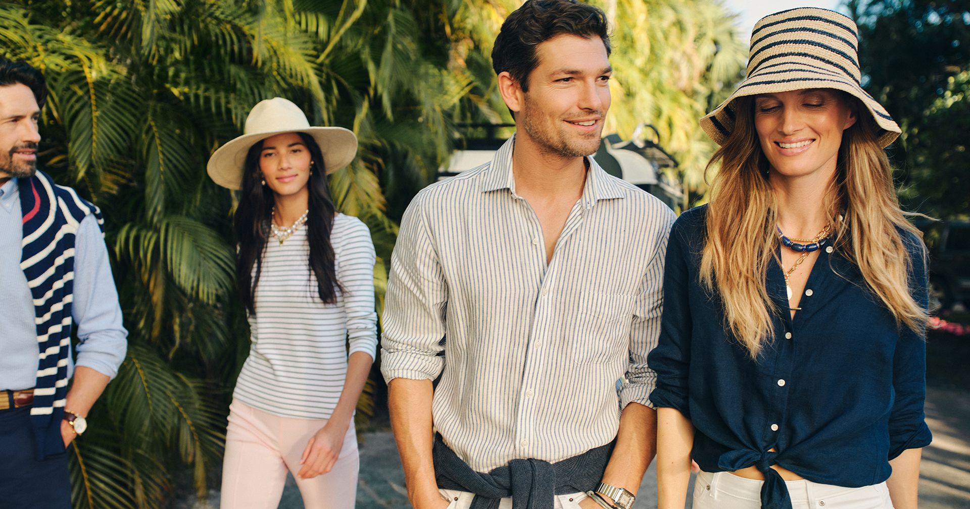 group of people walking outside in tropical environment. Man wearing stripe linen shirt and white jeans, women wearing navy linen shirt and white jeans