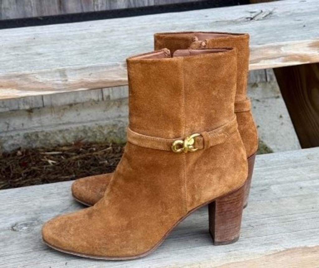 A pair of brown suede ankle boots with a gold buckle.