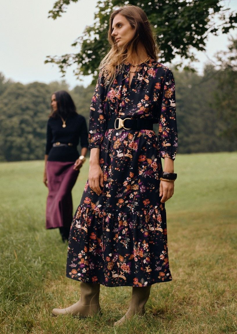 woman standing outside in a field wearing a black floral patterned long dress