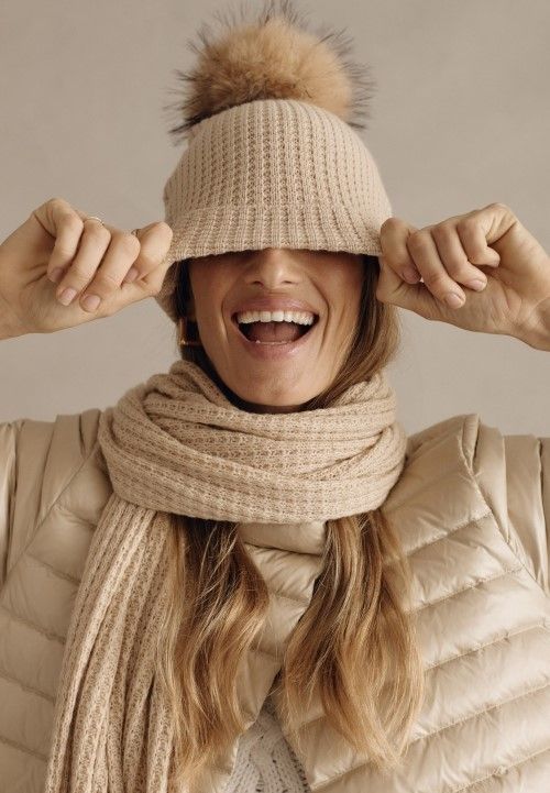 Close up image of woman in metallic golf puffer pulling tan pom pom hat down over her eyes